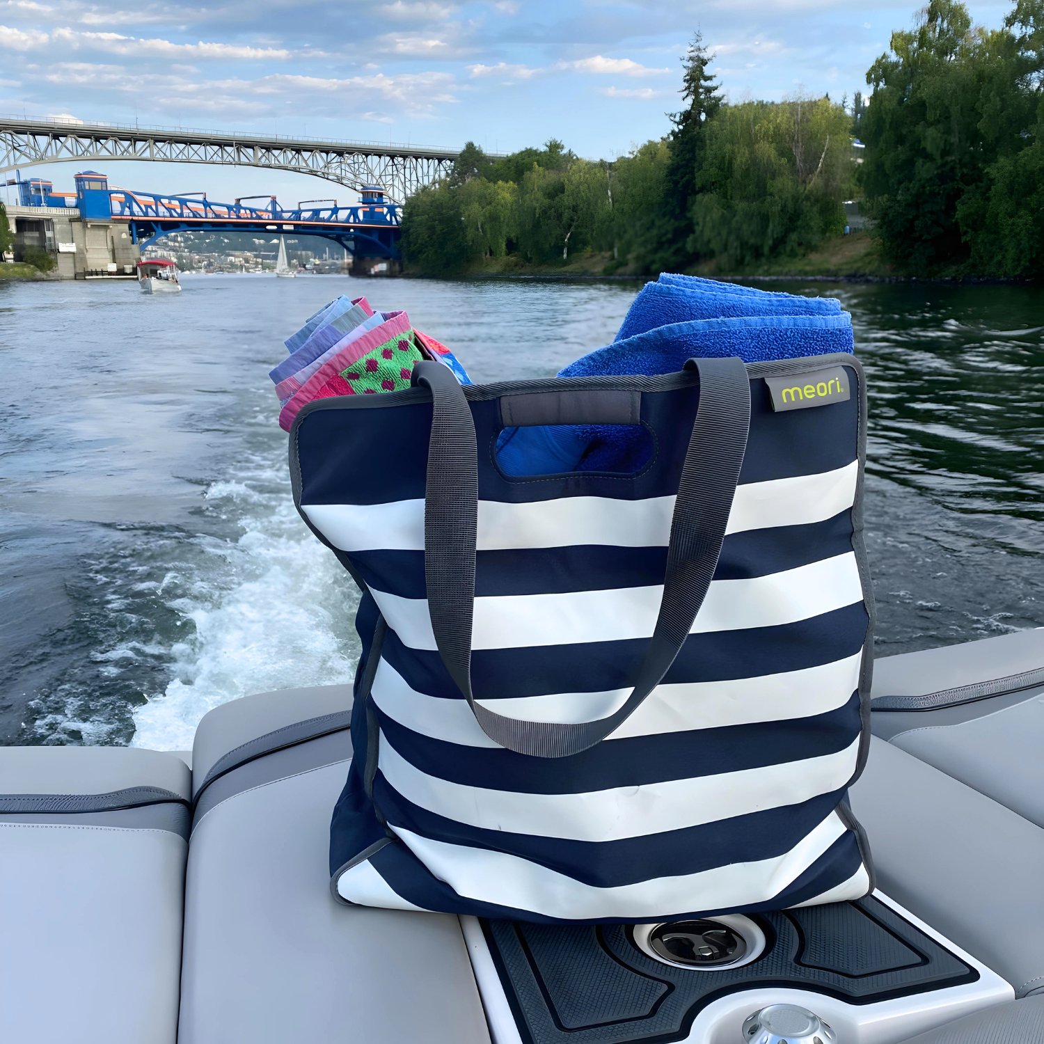A100351-11-meori-Large-Utility-Tote-Marine-Blue-Stripes-LST large utility tote on the back of a boat in the lake with bridge in the background