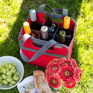 Red 6 Bottle Wine Tote filled with 6 wine bottles on lawn next to a bowl of grapes and a baguette.