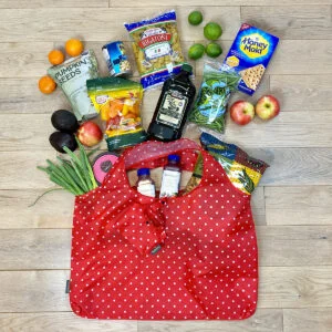 Red Grocery Bag with White Dots shown lying flat on floor with groceries spread around the bag