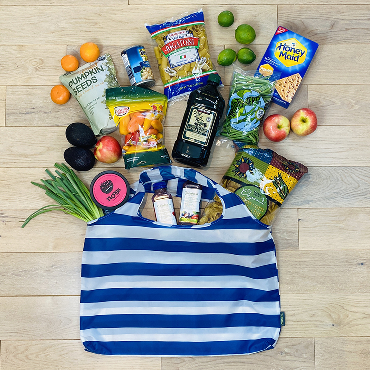 A100783-05-meori-Reusable-Pocket-Shopper-Classic-Blue-Stripes-LST Marine Blue Reusable Shopping Bag with White Stripes shown lying flat on floor with groceries spread around the bag