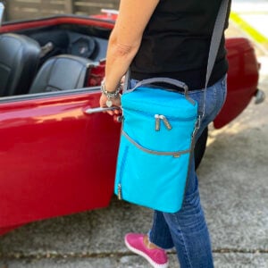 A100823-08-meori-Insulated-Wine-Tote-2-Bottles-Azure-Blue-LST Azure Blue 2 Bottle Insulated Wine Bag hanging over woman's shoulder on the side of red convertible