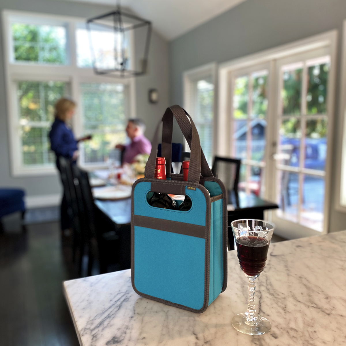 A100826-8-meori-2-Bottle-Wine-Tote-Azure-Blue-LST Red Wine Glas next to Azure Blue 2 Bottle Wine Carrier Tote filled with two bottles on kitchen counter