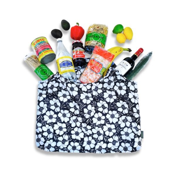 Black Reusable Grocery Bag with White Floral Print  shown lying flat on floor with groceries spread around the bag