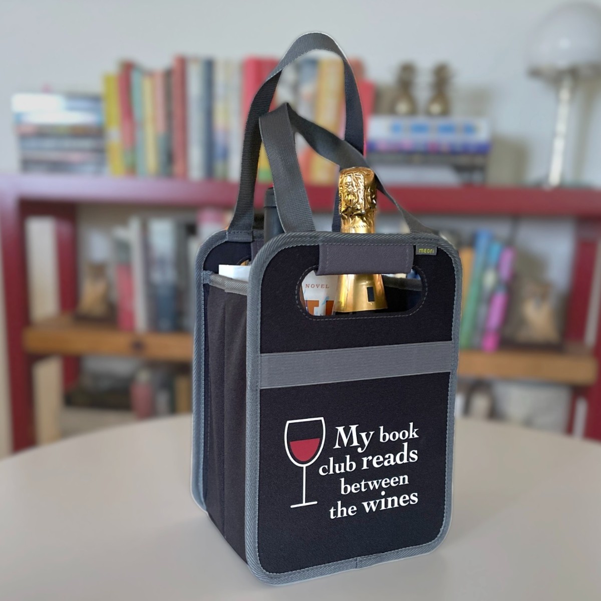A100873-06-meori-Book-Club-Wine-Tote-LST Black Book Tote Bag with two bottles and a book on table in front of bookshelf