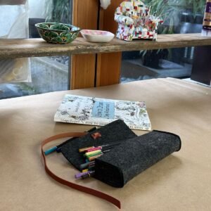 Open grey felt pouch with colorful pencil showing next to coloring book on craft table