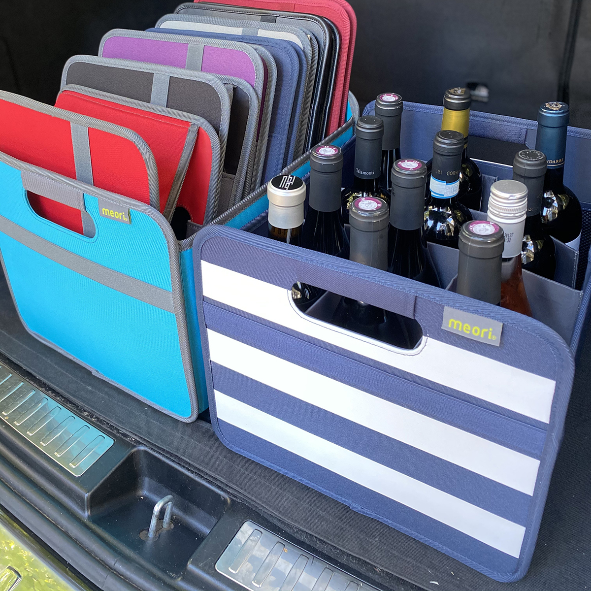B100792-11-meori-12-Bottle-Wine-Carrier-Marine-Blue-Stripes-LST Marine Blue 12 Bottle Wine Carry Bag with White Stripes filled with bottles in the back of a trunk next to a bin full with folded boxes